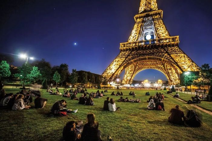 法国,巴黎| 夜晚,游客们坐在草坪上欣赏灯火通明的埃菲尔铁塔.