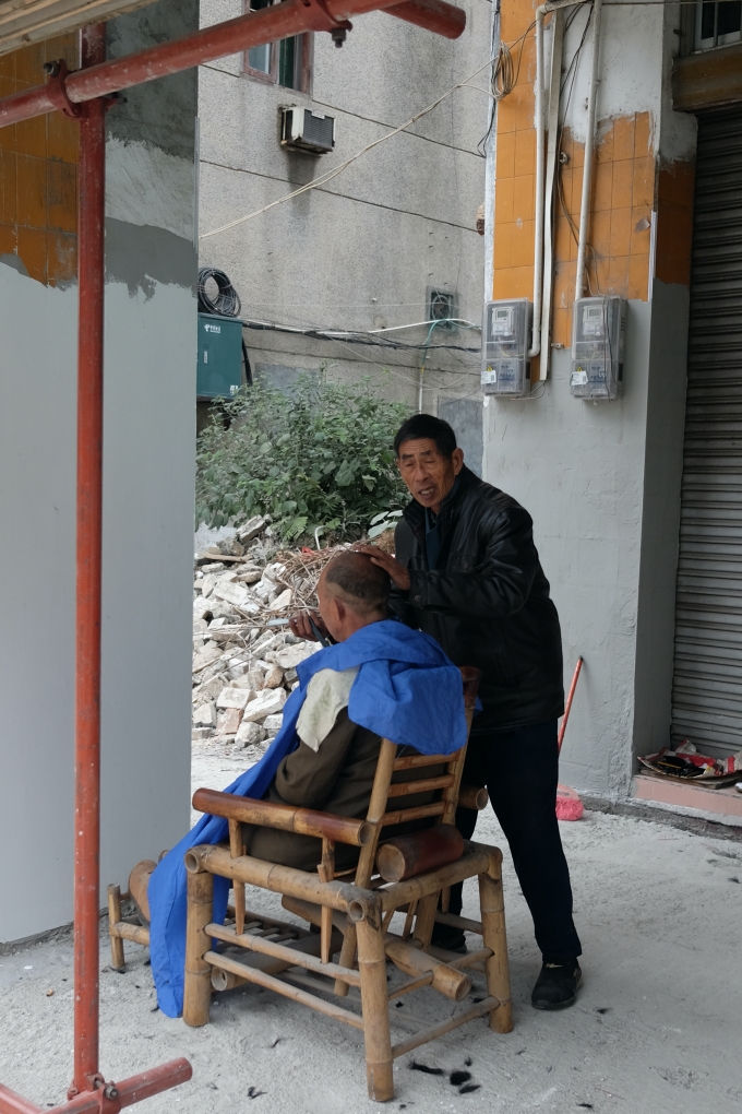 2019年12月1日上午，一位剃头师傅仍在脚手架下为顾客剔头。澎湃新闻记者 沈健文 图