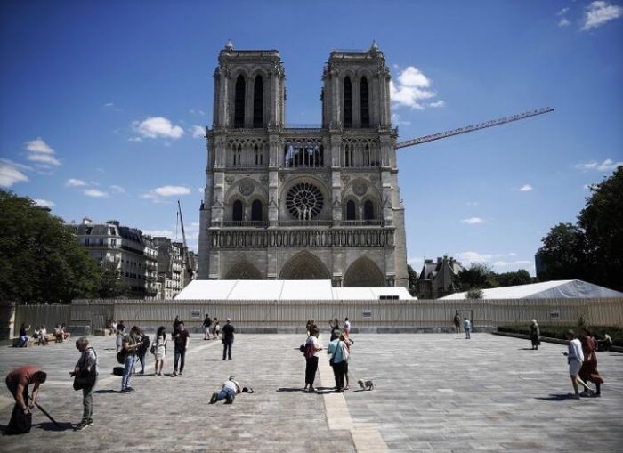 2019年4月，巴黎圣母院发生严重火灾，数小时内释放出数十吨含铅粉尘，教堂前庭因铅污染而被迫关闭，这是时隔一年来首次向公众开放。建筑工人们目前正在移除教堂外部的支撑脚手架，下一步是建造防雨临时屋顶。圣母院正式重建工程要到2021年才会开始，法国总统承诺一定会在2024年巴黎奥运会前完成重建。（摄影师：Yoan Valat）